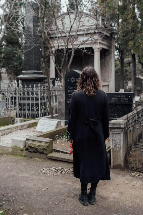 Woman standing on a pathway looking at a grave from afar