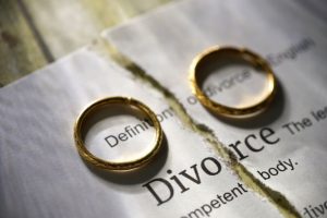 Zwei Eheringe auf einem gespaltenen Papier mit dem Wort Scheidung darauf.
